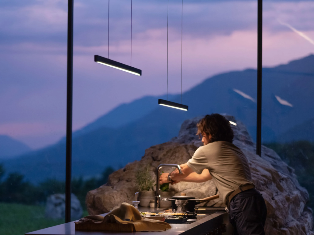 BORA STARS Horizon viseća lampa iznad kuhinjskog ostrva, stvara toplu atmosferu uz pogled na planine i prirodno kamenje u enterijeru.